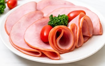 Rökt skivad skinka på en tallrik med körsbärstomater och lite dill