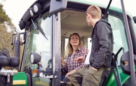 Ung man pratar med bonde i hennes traktor.